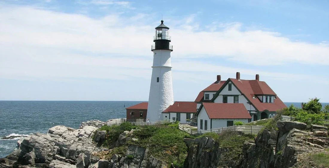 Leuchtturm mit Häusern auf einem Felsen vor dem Meer in Neuengland